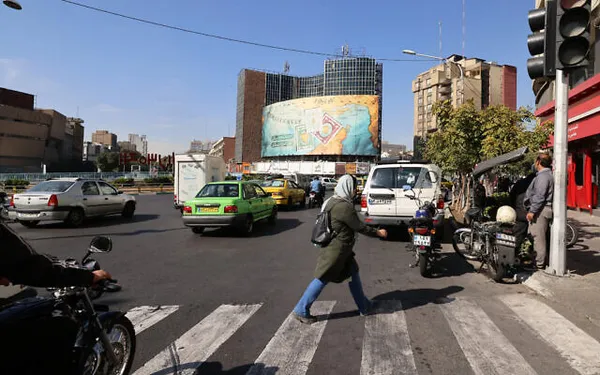 People walk and drive past a billboard covering the facade of a building on Vali-Asr square in Tehran, Iran, October 26, 2024. (Atta Kenare/AFP)